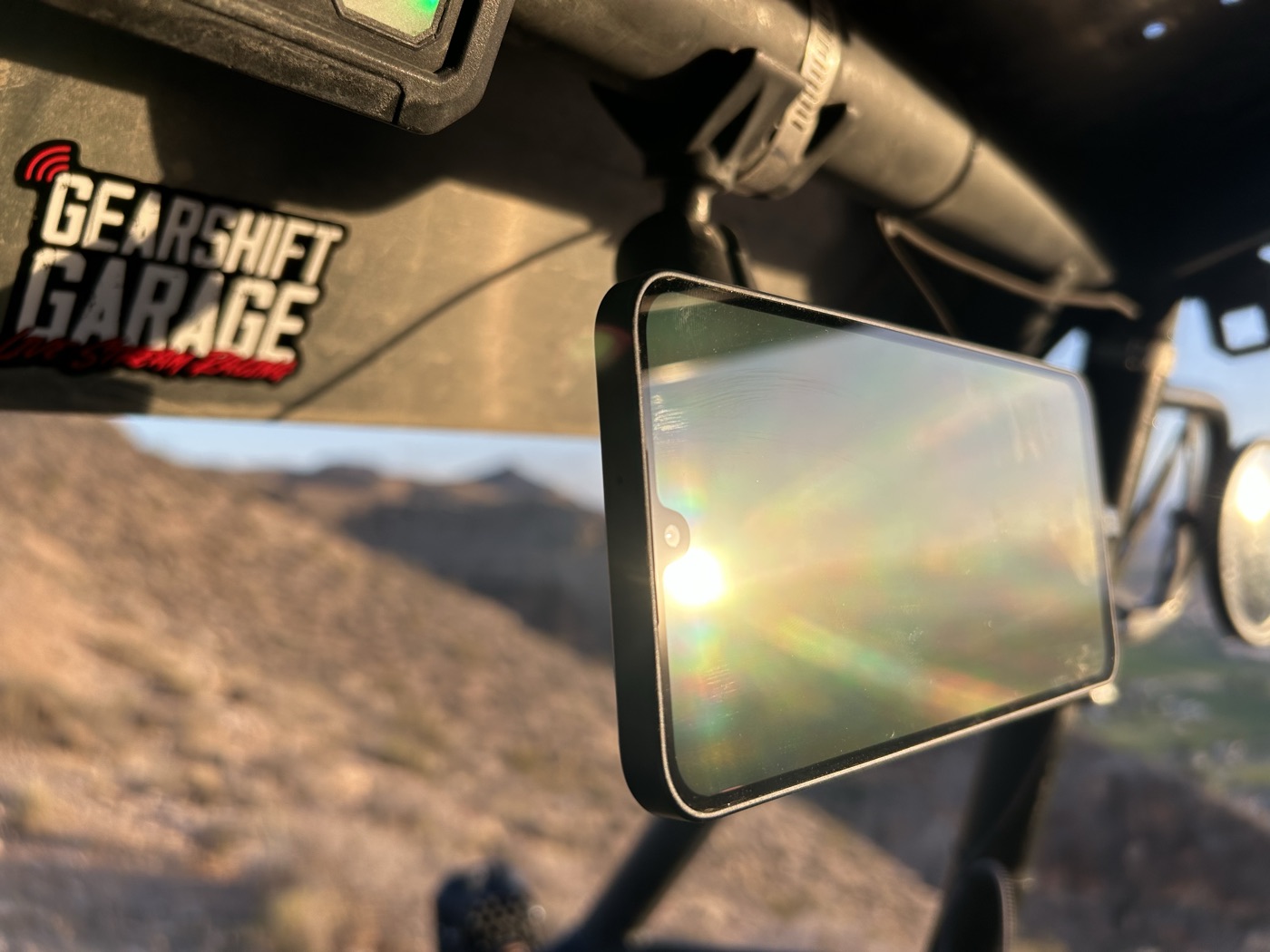 A phone mounted in a UTV cockpit running the tracking screen, desert visible through the windscreen